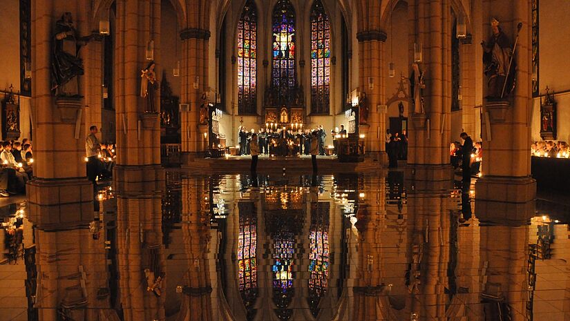 Auf dem Boden im Kirchraum ist Wasser, sodass sich das Licht um den Altar spiegelt