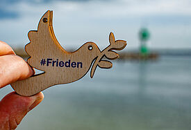 Eine Hand hält eine kleine Pappelholztaube mit dem Aufdruck #Frieden