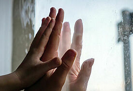 Hände berühren sich getrennt durch eine Glasscheibe.