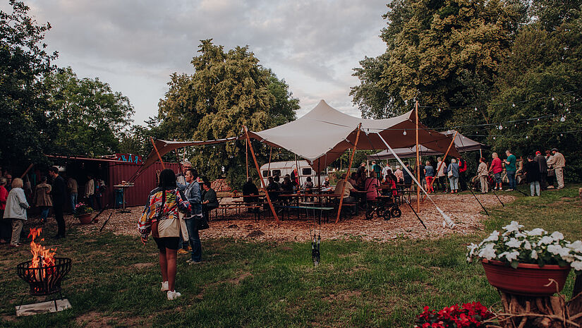 Ein großes Sonnensegel in einer Grünfläche, rundherum Ausstattungsstücke für das Festival.