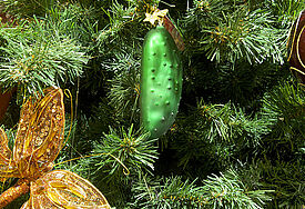 Eine grüne Weihnachtsgurke aus Glas hängt an einem geschmückten Baum.