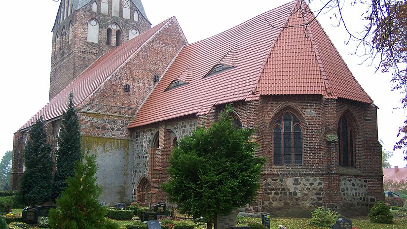 Backsteinkirche, umgeben von kleinen Bäumen und Friedhof