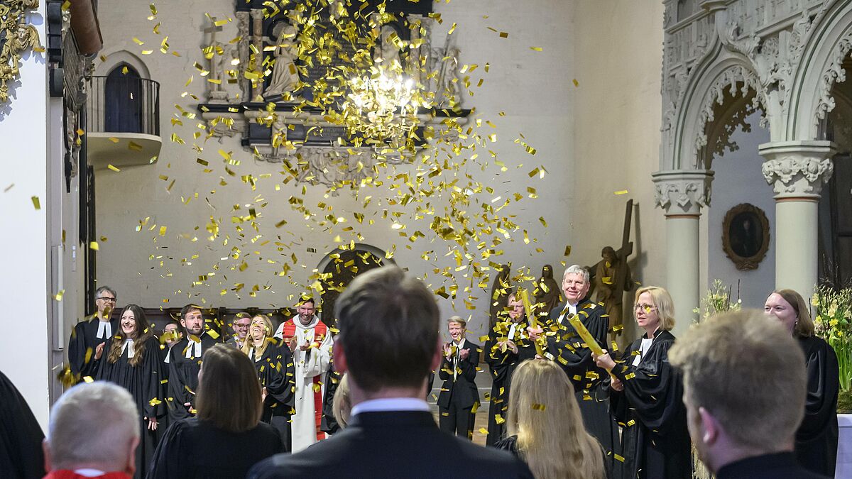 Oberkirchenrat Wolfgang Boten aus dem Landeskirchenamt Kiel und Bischöfin Nora Steen lassen Gold auf die neuen Pastorinnen und Pastoren im Sprengel Schleswig und Holstein regnen.