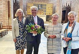 Synoden-Präses Katrin Thomas (v.li), Pröpstin Petra Kallies und Bischöfin Kirsten Fehrs gratulieren Philip Graffam, der einen Blumenstrauß in Händen hält,  nach der Wahl im Ratzeburger Dom. 