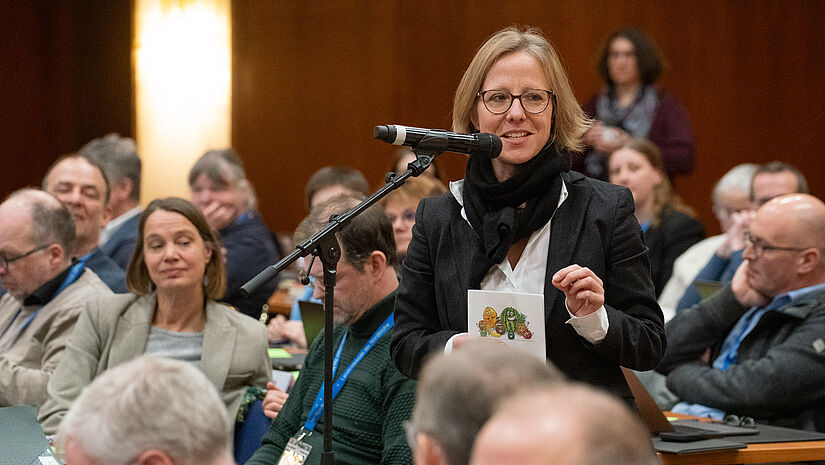 Eine Frau steht in einem Plenum am Mikrofon und äußert sich 