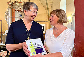 Grund zur Freude: Die Vorsitzende des Fördervereins zum Erhalt der Dorfkirche Zahrensdorf erhält aus den Händen von Schirmherrin Kristina Kühnbaum-Schmidt die Plakette „Dorfkirche mon amour Kulturkirche“. 