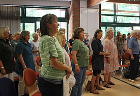 In mehreren Stuhlreihen stehen Frauen und singen