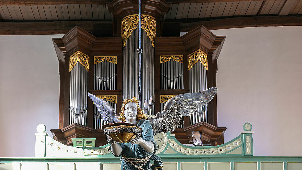 Vor der Orgel der St. Marienkirche in Gudow in Schleswig-Holstein hängt ein hölzerner Taufengel von der Decke.