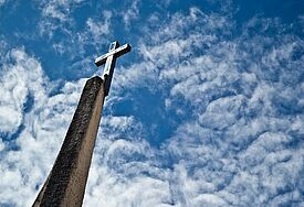 Kreuz, das in den blauen Himmel mit Altocumulus-Wolken ragt