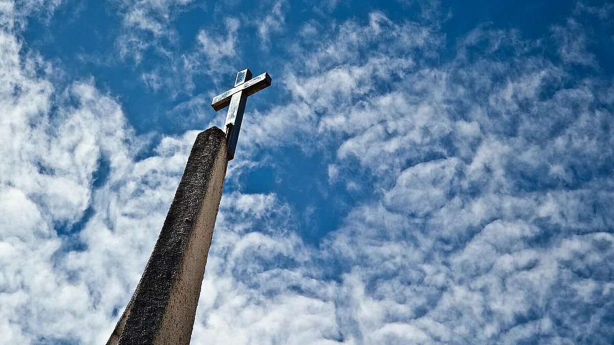 Kreuz, das in den blauen Himmel mit Altocumulus-Wolken ragt