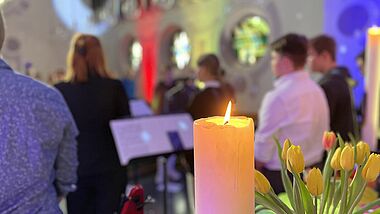 Blick auf Jugendliche von hinten in einem Jugendgottesdienst, vorne eine Kerze und ein Blumenstrauß in einer Vase