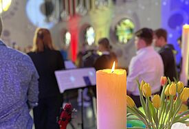 Blick auf Jugendliche von hinten in einem Jugendgottesdienst, vorne eine Kerze und ein Blumenstrauß in einer Vase