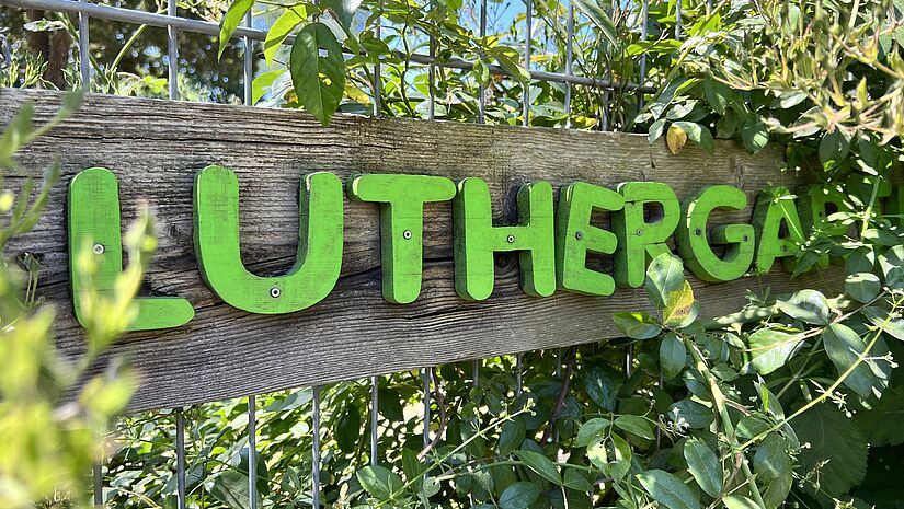 In grünen Buchstaben steht Luthergarten am Zaun neben dem Eingang zum Garten.