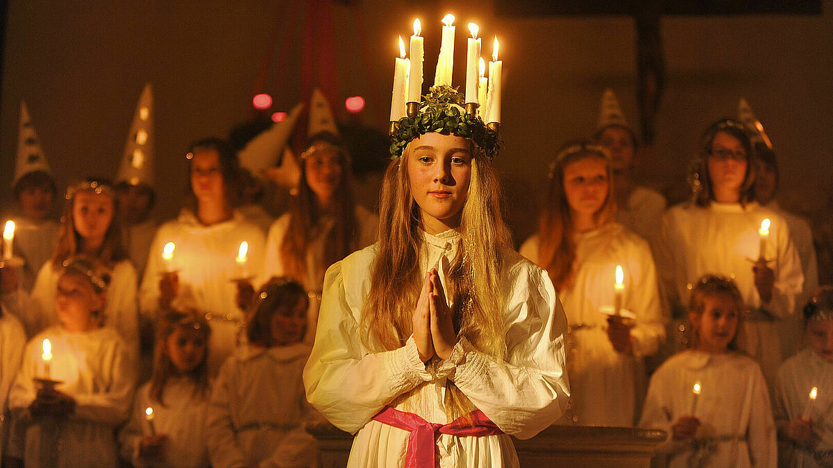 Die Schutzheilige Lucia trägt ein weißes Gewand und einen Lichterkranz.