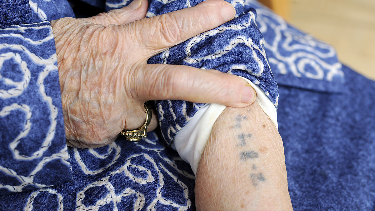 Auschwitz-Überlebende zeigt ihren Oberarm mit tätowierter Häftlingsnummer.