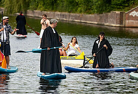 Pastorinnen und Pastoren der Pop Up Church unterwegs im Talar auf Stand Up Boards auf der Alster.
