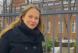 Pastorin Sandra Starfinger steht vor einem Zaun aus Metall. Hinter dem Zaun  die aus roten Backsteinziegeln gemauerte St. Pauli-Kirche.