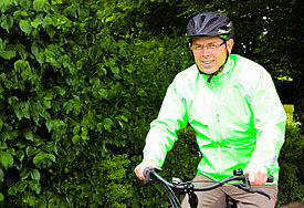 Der Bischof sitzt mit Helm und grüner Regenjacke auf dem Fahrrad