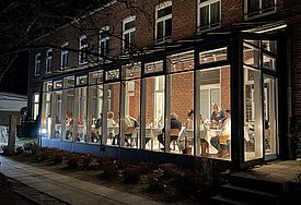 Ein gläserner Wintergarten, in dem Menschen an Tischen sitzen