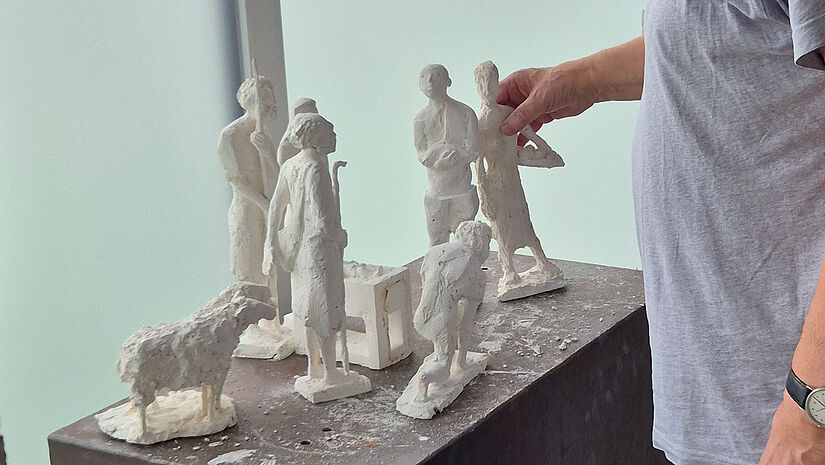Ein Mann fasst eine Krippenfigur aus Gips an. Sie steht mit anderen Figuren auf einem Podest.