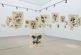 Das Kunstwerk Einwanderung von Künstlerin Sybille Loew:56 auf Leinwand gestickte Portraits von Menschen mit Migrationshintergrund hängen von der Decke der Galerie. Auf Augenhöhe montiert, man sieht sie von Angesicht zu Angesicht.