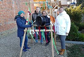 Pastorin Barbara Häußler (mit Kochlöffel) und Frau Schäfer (rechts) vor dem Gestell mit Felge. Hinten: Pastor Kark-Carlson mit Ehefrau Kathrin Kark