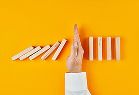 Hand, die umfallende Dominosteine unterbricht 
