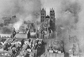Blick auf die Lübecker Altstadt aus einem Flugzeug. Rauch steigt auf, Häuser sind zerstört.