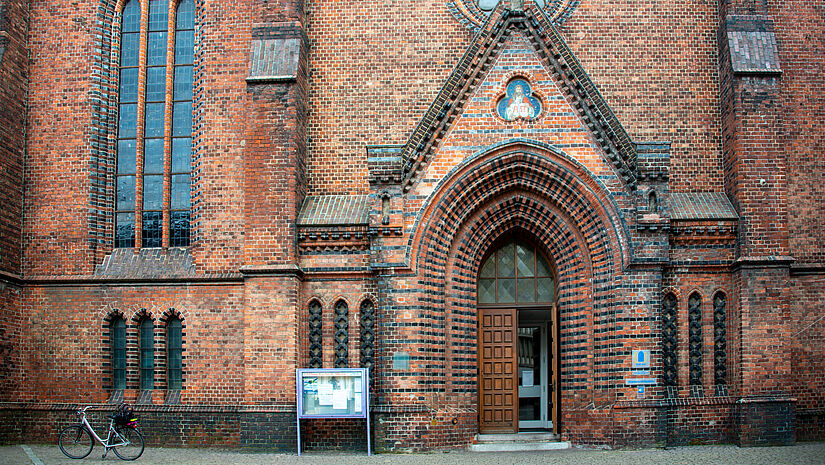 Eingang der St. Nikolaikirche in Kiel. Die Tür steht offen, ein Fahrrad ist vor der Kirche abgestellt.