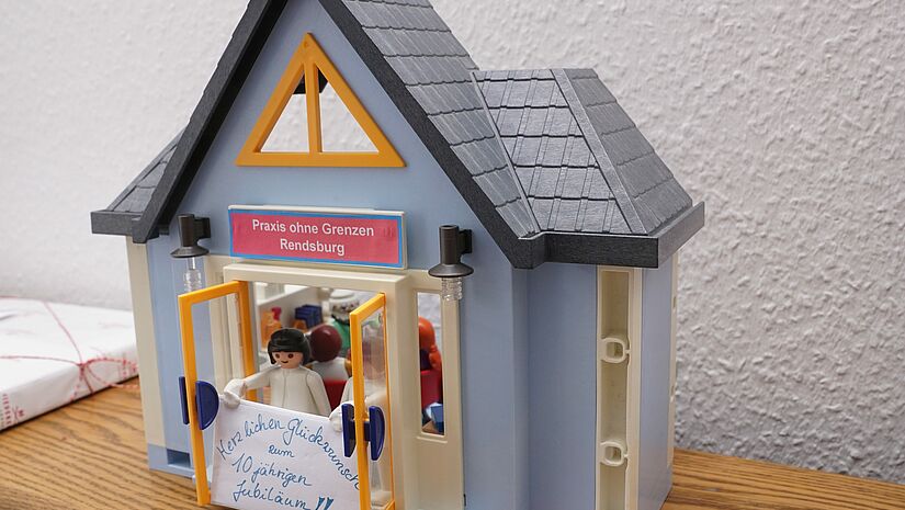 Die "Praxis ohne Grenzen" kümmert sich seit 2013 um Menschen, die durch die Lücken im Versorgungsnetz gefallen sind. Das medizinische Personal arbeitet ehrenamtlich. Playmobilhaus mit Schild "Praxis ohne Grenzen"
