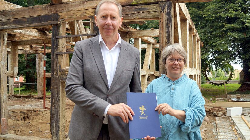 Die Pastorin der Kirchengemeinden Benz und Morgenitz, Annegret Möller-Titel, freute sich auf der Baustelle der Pfarrscheune in Liepe über den Fördermittelbescheid, den ihr Heiko Miraß, Parlamentarischer Staatssekretär für Vorpommern und das östliche Mecklenburg, überreichte.
