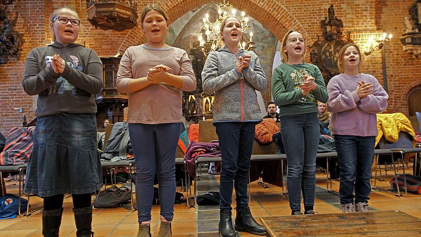 Die St. Nicolai Girls – ein Kinderchor der Kirchengemeinde Eckernförde. Fünf Mädchen stehen singend nebeneinander in der Kirche.