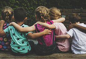 Kinder sitzen Arm in Arm im Gras (Rückenansicht) 