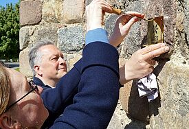 Gemeinsam befestigten Anett Burckhardt, Baubeauftragte des Pommerschen Evangelischen Kirchenkreises, und Klaus-Martin Bresgott, Mitglied des Kulturbüros der EKD, am Freitag, 6. Mai, an der Pasewalker Nikolaikirche die Plakette des EKD-Projekts „Land:Gut 2022“. 
