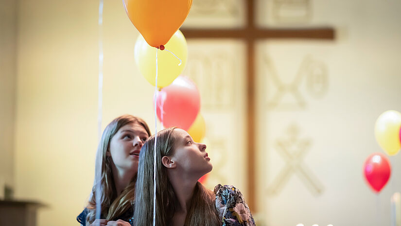 Zwei Mädchen stehen in einer mit bunten Luftballons geschmückten Kirche.