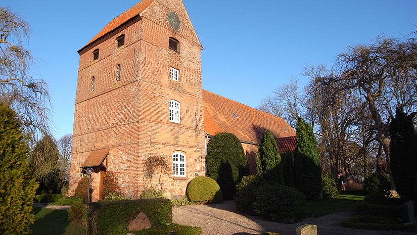 Backsteinkirche in Waabs, blauer Himmel, umgeben von Bäumen