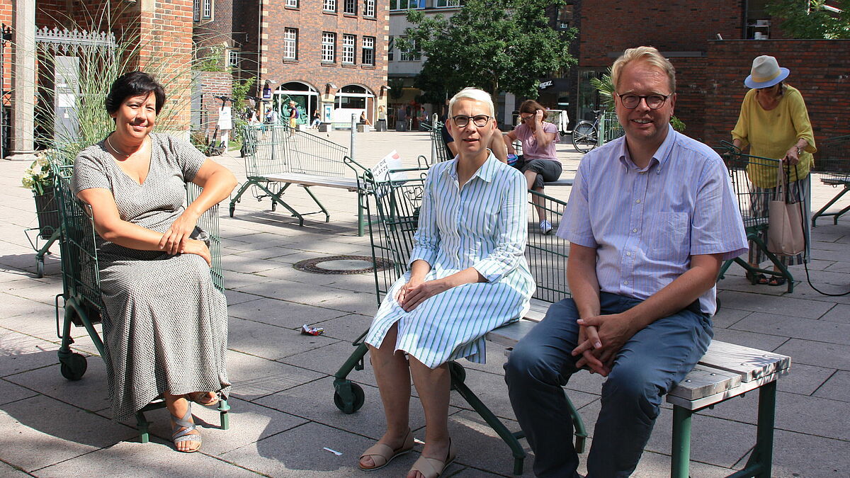 Jacobi-Pastorin Lisa Tsang, Petri-Pastorin Gunhild Warning und Petri-Hauptpastor Jens-Martin Kruse sitzen auf dem Platz vor der Petrikirche in der Hamburger Innernstadt.
