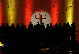 Weihnachtskonzert mit Popchören in Kiel Schatten eines Chores in einer gelb-rot beleuchteten Kirche. An der Wand hängt ein Kreuz.