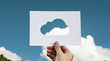 Eine Hand hält eine Wolkenschablone gegen den blauen Himmel