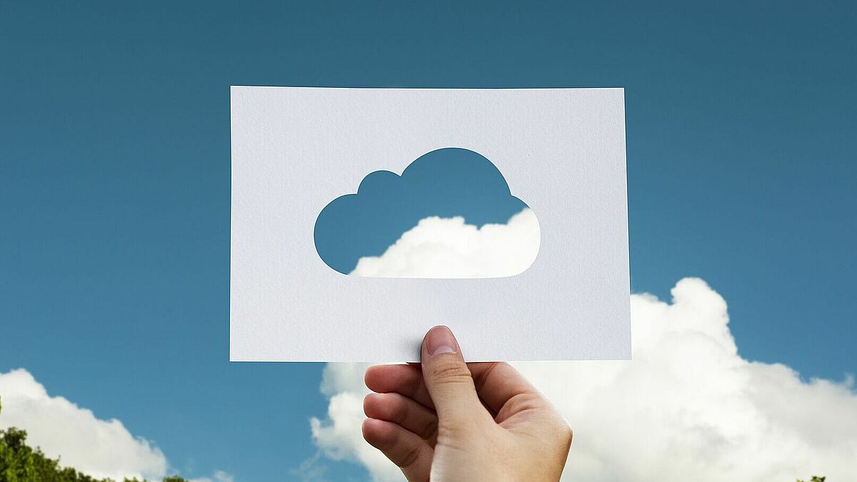 Eine Hand hält eine Wolkenschablone gegen den blauen Himmel