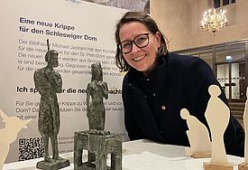 Eine Frau beugt sich über die Krippenfiguren Maria, Josef und dem Jesuskind