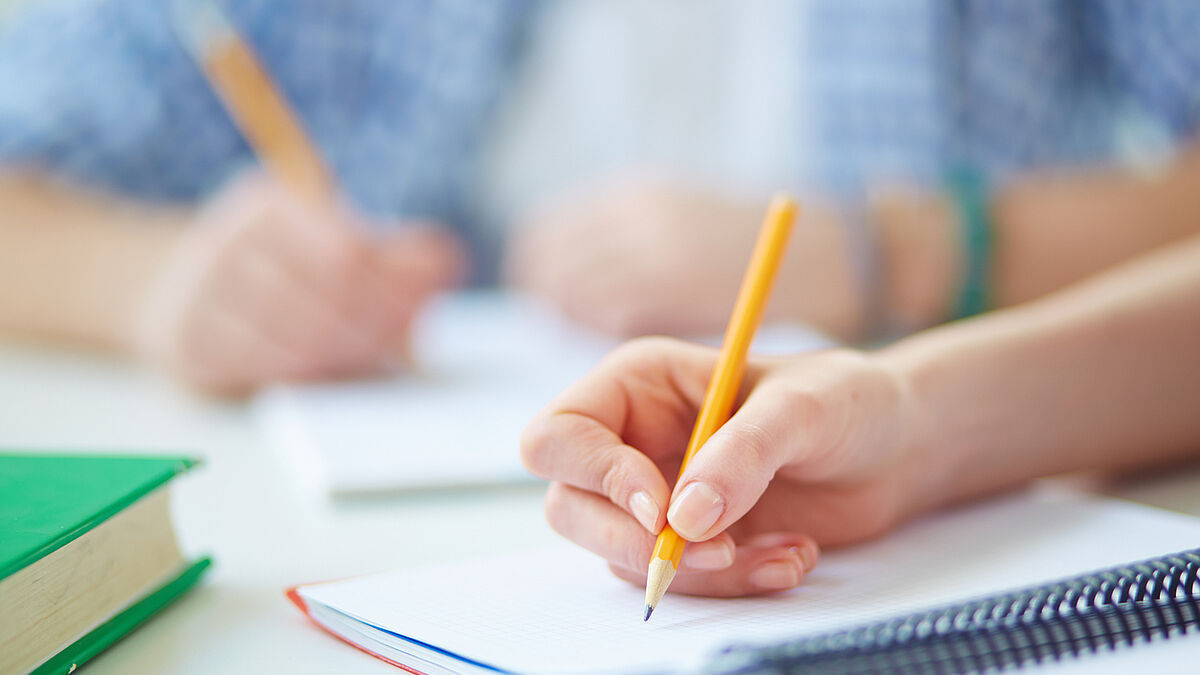 Hand of student with pencil carrying out written task or writing lecture