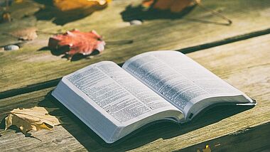 Bibel auf einem Holztisch, draußen, umgeben von ein paar Laubblättern
