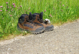 Feldflasche und Wanderschuhe am Wegesrand