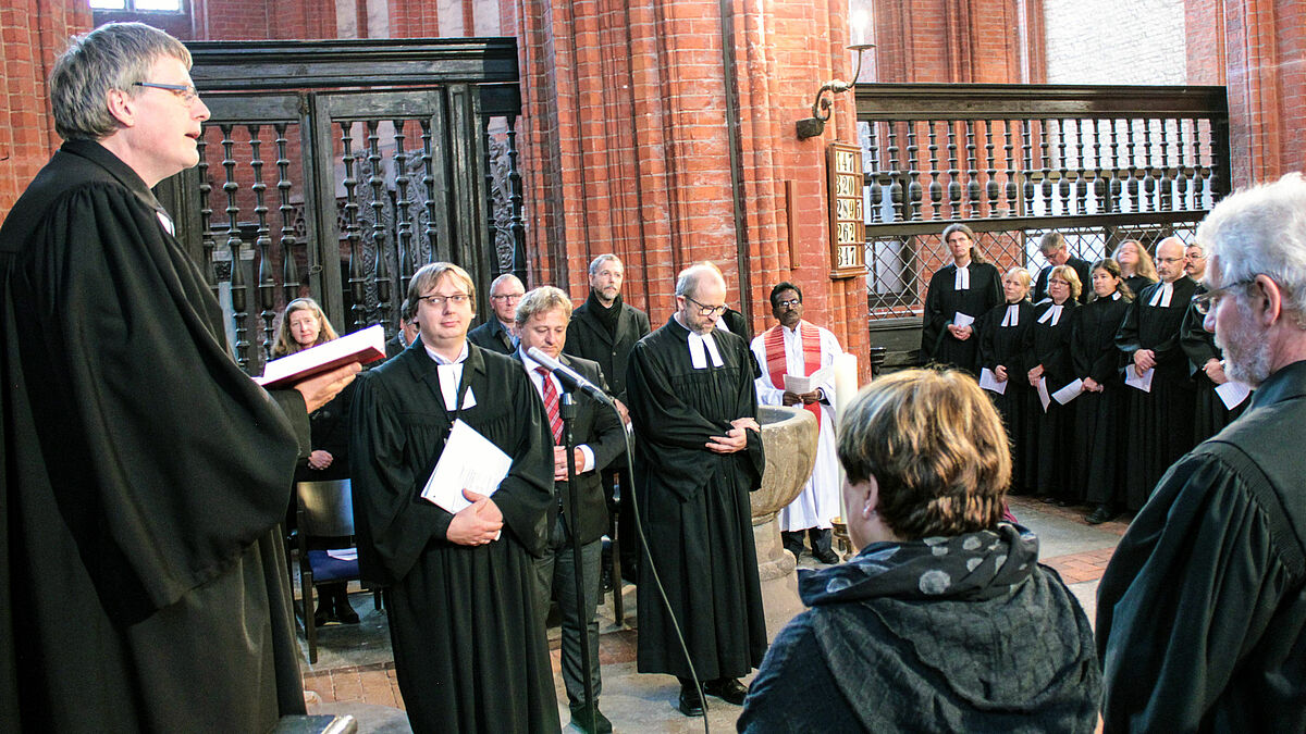 Bischof Dr. Andreas v. Maltzahn (l.) führt Marcus Antonioli (2.v.l.) ein und übergibt das Amtskreuz in der St. Nikolai-Kirche Wismar.