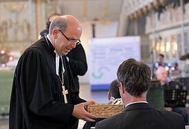 Bischof Magaard reicht einen Korb mit Segensbändchen in die Reihen der Gottesdienstbesucher