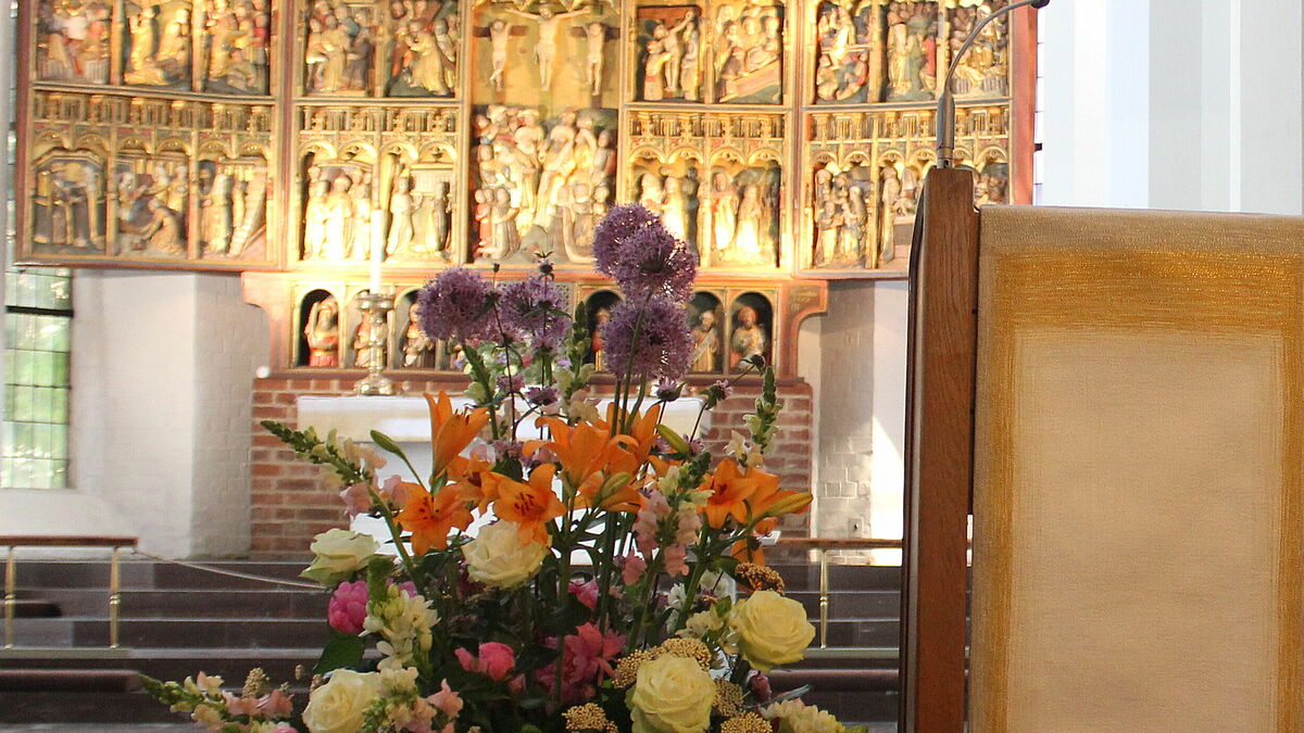 Blick in den Chorraum der Nikolaikirche in Kiel, im Vordergrund Blumen und Lesepult