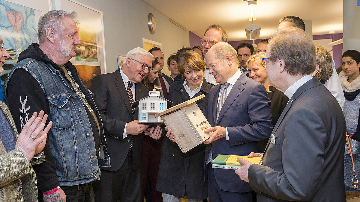 Bei seinem Besuch in der Einrichtung "Herz As" erhält Bundespräsident Frank-Walter Steinmeier (2. v.l.) ein selbst gefertigtes Vogelhäuschen aus der "Herz As"-Werkstatt, das seinem Amtssitz Schloss Bellevue nachempfunden ist.