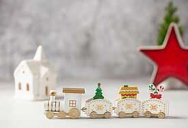 Ein weißer Spielzeug-Zug aus Holz transportiert einen Tannenbaum, ein Haus und ein Geschenk.