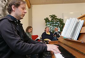 Das Foto zeigt Jan Simowitsch am Klavier beim Begleiten eines der neuen Lieder. Im Hintergrund rechts Propst Matthias Krüger, neben ihm sitzt Pastorin Kerstin Hansen Neupert.